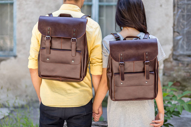 Back of woman and man with brown leather backpack. Man and woman holding hands and presenting leather bags. Unisex bag for sale. - Photo, Image