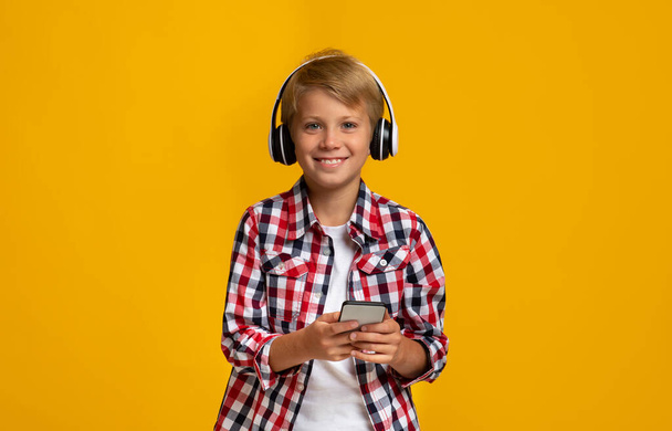 Ευτυχισμένος Ευρωπαίος έφηβος αγόρι στα ακουστικά κρατώντας smartphone, παρακολουθήστε το μάθημα βίντεο - Φωτογραφία, εικόνα