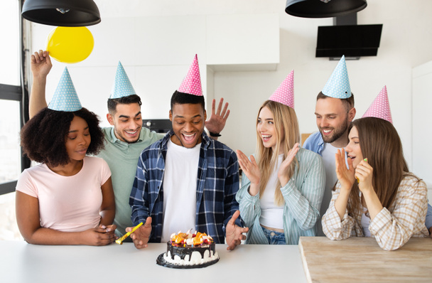 Opgewonden zwarte man ontvangt verjaardagstaart van zijn interraciale vrienden, vieren b-dag thuis - Foto, afbeelding