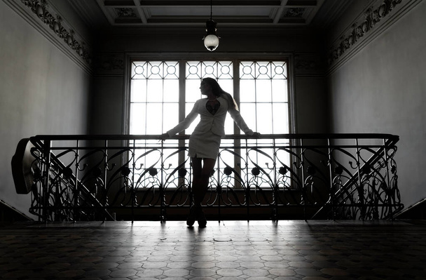 Woman in short skirt near iron stairs. Portrait full length of beautiful young adult slim aucasian woman standing against old window. - Foto, Imagen