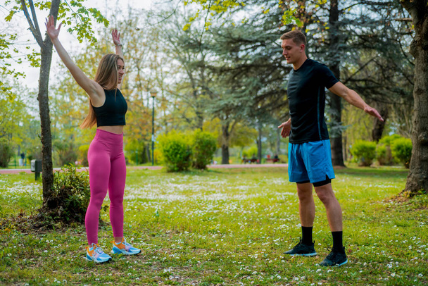 Ζευγάρι τεντώνει τους μυς στο πράσινο γρασίδι στο πάρκο. Αθλητής κάνει προπόνηση σε εξωτερικούς χώρους. Αθλητισμός, γιόγκα, pilates, fitness, έννοια του υγιεινού τρόπου ζωής - Φωτογραφία, εικόνα