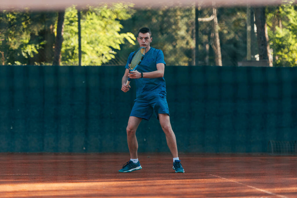 Fuerte jugador de tenis masculino observado a través de la red de tenis - Foto, Imagen
