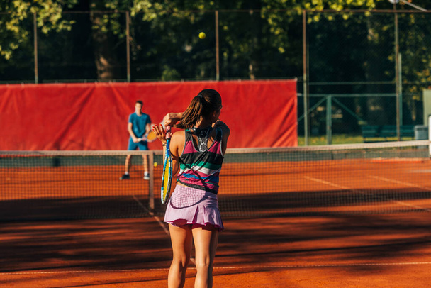 View from the back of a young female paying tennis on a court outside - Photo, Image