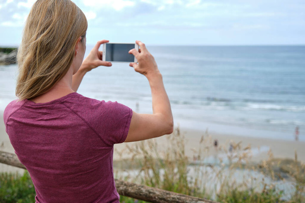 Жінка фотографує з камерою смартфона на пляжі, вид ззаду
. - Фото, зображення