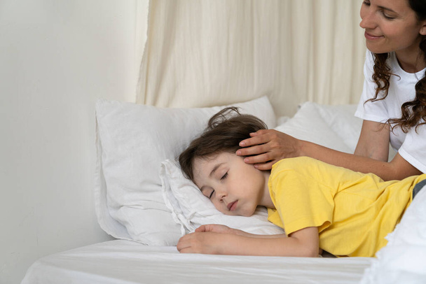 Cuidar madre acariciando la cabeza del niño hijo durmiendo en la cama en la mañana despertar tiernamente niño preescolar - Foto, imagen