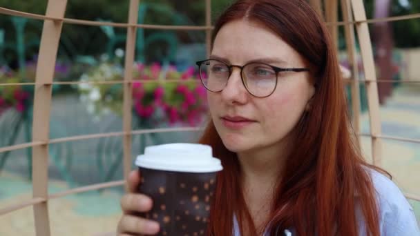 Close up of young woman holding paper cup of coffee and enjoy drink at the street, take away. Business woman in stylish shirt and eyesight glasses - Footage, Video