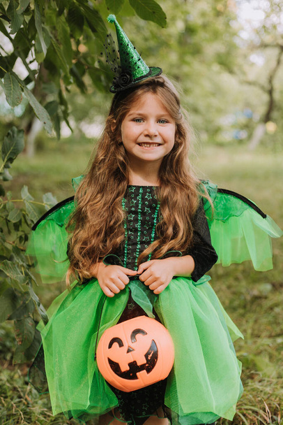 Słodka dziewczynka w stroju czarownicy na Halloween trzymając kosz dyni w parku. Dziecko na świeżym powietrzu. Cukierek albo psikus. Koncepcja Halloween - Zdjęcie, obraz