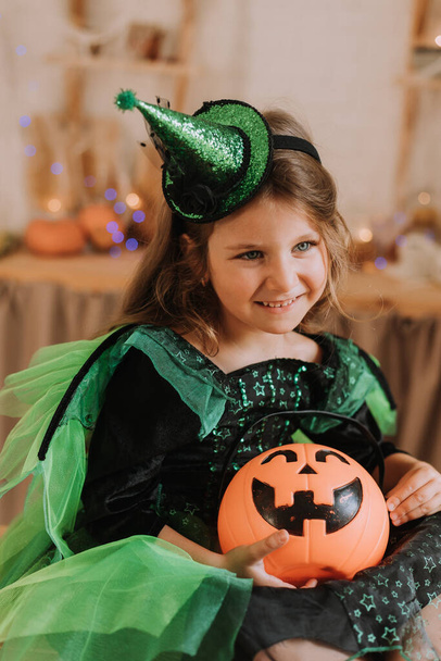 Pieni tyttö karnevaali Halloween puku istuu keittiössä. Kurpitsalyhty-Jack, kori makeisille. Karkki tai kepponen.  - Valokuva, kuva