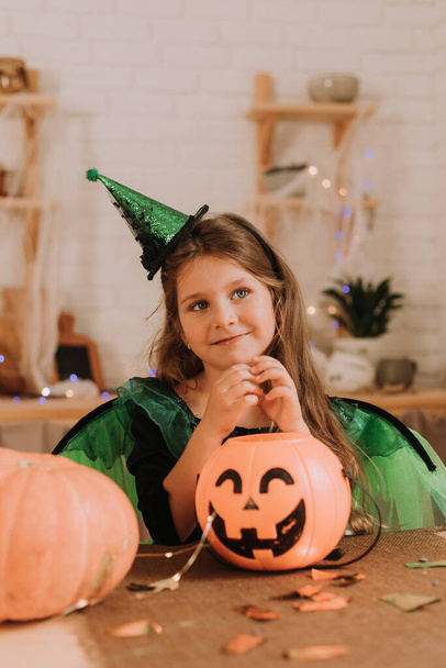 Bambina in costume di Halloween carnevale sdraiata in cucina. Lanterna di zucca Jack, cesto per dolci. Dolcetto o scherzetto.  - Foto, immagini