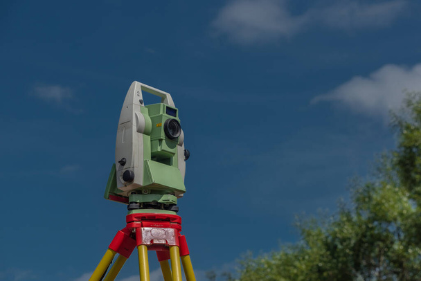 Stroj pro zeměměřiče s modrou oblohou a zelenými stromy ve slunečný barevný den - Fotografie, Obrázek