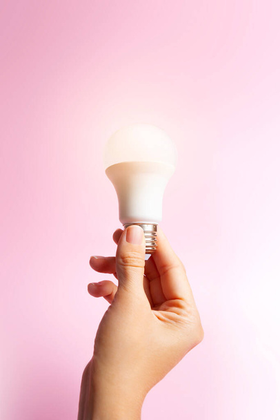 woman's hand grasping a lit light bulb. pink background. Idea concept. - Photo, Image