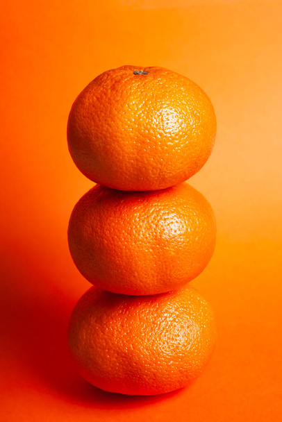 3 naranjas colocadas una encima de la otra en un plano cerrado y un fondo del mismo color naranja. Concepto comida real - Foto, imagen