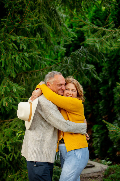 літня пара обіймається на тлі соснових дерев
  - Фото, зображення