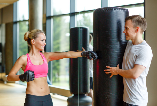 smiling woman with personal trainer boxing in gym - Fotó, kép