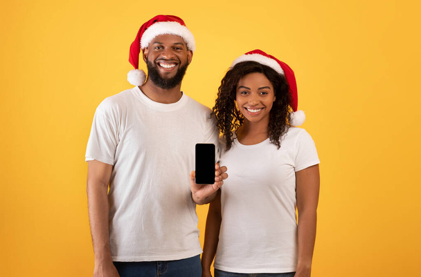 Boldog afro-amerikai házastársak mutatja okostelefon üres képernyőn sárga háttér, mockup - Fotó, kép