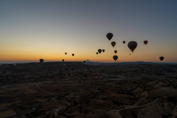 Cappadocia, Turkey - September 14, 2021: Wide angle aerial shot of colorful hot air balloons together floating in the sky at early morning sunrise horizon in Goreme national park - Photo, image