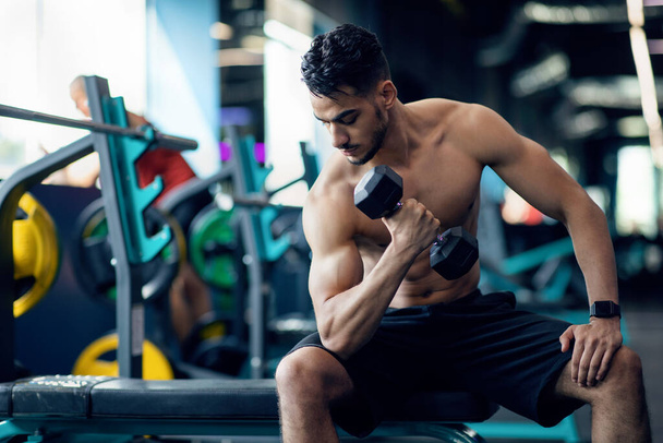 Muskulöser Araber mit nacktem Oberkörper macht Übungen mit Kurzhanteln im Fitnessstudio - Foto, Bild