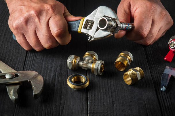Klempner verbindet Messingbeschläge mit einem verstellbaren Schraubenschlüssel. Nahaufnahme der Hand des Meisters bei der Arbeit in der Werkstatt - Foto, Bild
