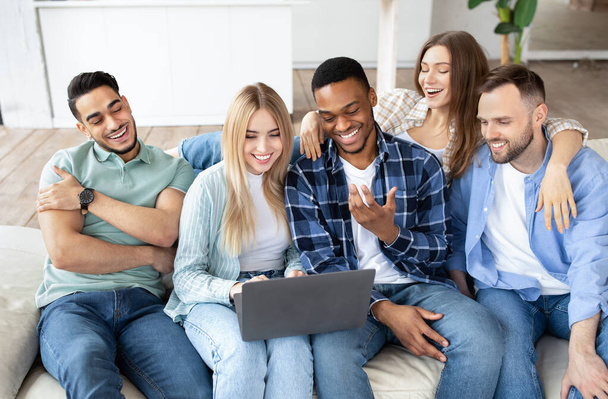 Χαρούμενοι διαφορετικοί φίλοι που χρησιμοποιούν φορητό υπολογιστή, κάθονται σε καναπέ στο σαλόνι, έχοντας βιντεοκλήση, κουβεντιάζοντας online στο σπίτι - Φωτογραφία, εικόνα