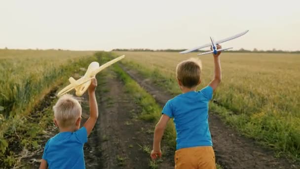 Jungen, Kinder, die im Park durch ein Weizenfeld rennen, spielen mit einem Spielzeugflugzeug in der Hand, träumen vom Fliegen. Kind spielt mit seinem Spielzeug mit Flugzeug. Kinderfreunde rennen, träumen, arbeiten, reisen. Glücklicher Familientag - Filmmaterial, Video