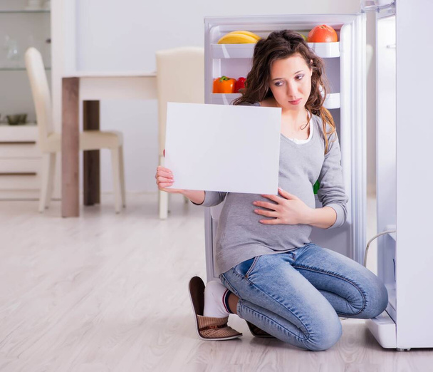 Έγκυος γυναίκα κοντά στο ψυγείο με κενό μήνυμα - Φωτογραφία, εικόνα