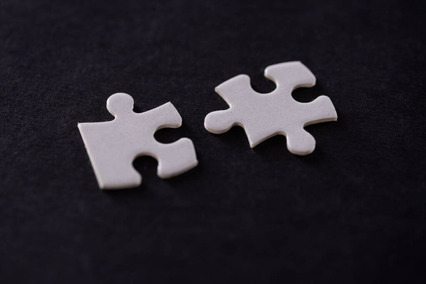 Two white jigsaw puzzles isolated on black background. - Foto, Imagen