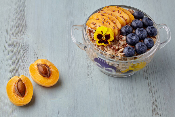 Whole grain oat flakes in a glass bowl with blueberries, apricot slices, flax seeds - Foto, afbeelding