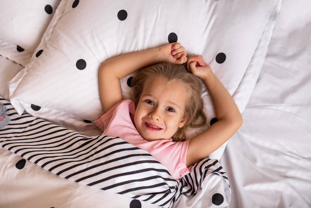 a beautiful little girl in pajamas is lying on cotton bed linen on the bed - Foto, Imagem