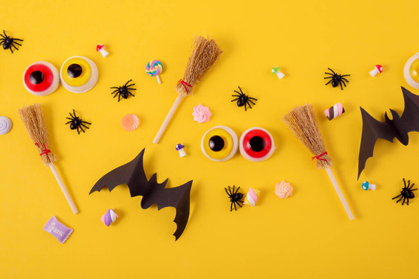 Halloween frame met pompoenen, spinnen en papier uitgesneden vleermuizen tegen een felgele achtergrond. Enge ogen en heksen bezems op een Top view Halloween concept. - Foto, afbeelding