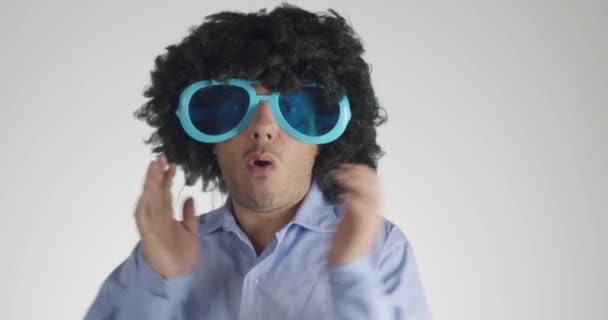 Man with curly hairy wearing funny and big sunglasses dancing with hands isolated on gray background. Party, music, lifestyle, radio and disco concept. - Footage, Video