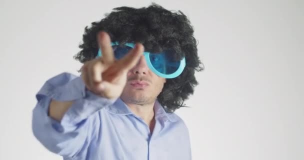 Man with curly hairy wearing funny and big sunglasses dancing showing victory sign isolated on gray background. Party, music, lifestyle, radio and disco concept. - Footage, Video