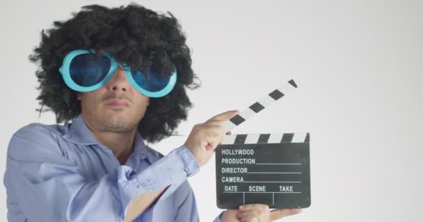 Man met krullend harig dragen grappig en grote zonnebril met behulp van een clapper geïsoleerd op grijze achtergrond. - Video