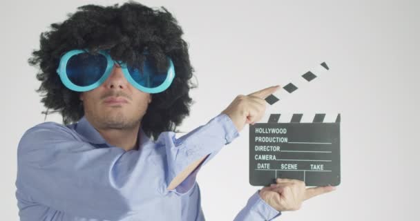 Mann mit lockigem Haar trägt lustige und große Sonnenbrille mit einem Klöppel isoliert auf grauem Hintergrund. - Filmmaterial, Video