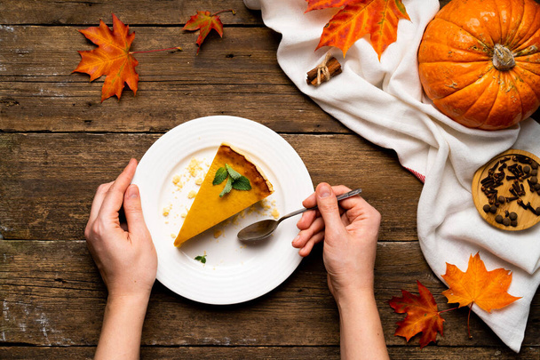 a piece of pumpkin pie on a wooden table with female hands, pumpkin and autumn leaves. - Photo, image