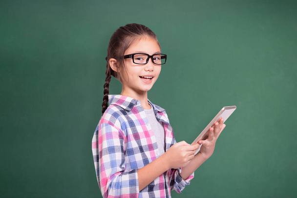 Chica estudiante feliz con gafas usando tablet.Isolated sobre fondo de pizarra verde. - Foto, imagen