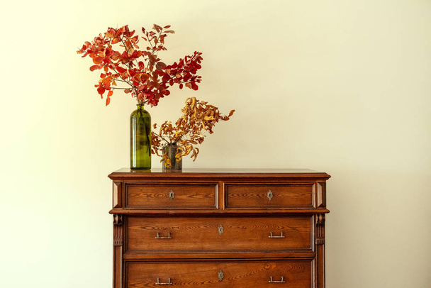 Wooden chest of drawers with floral branches in vase - Фото, зображення