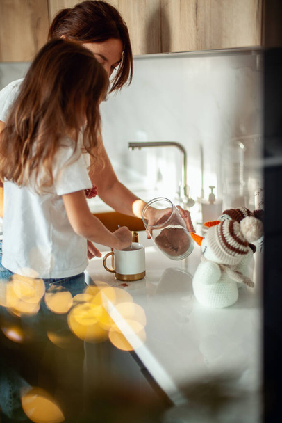 A young beautiful mother and a crying daughter are preparing cocoa in a stylish home kitchen. - Foto, Bild