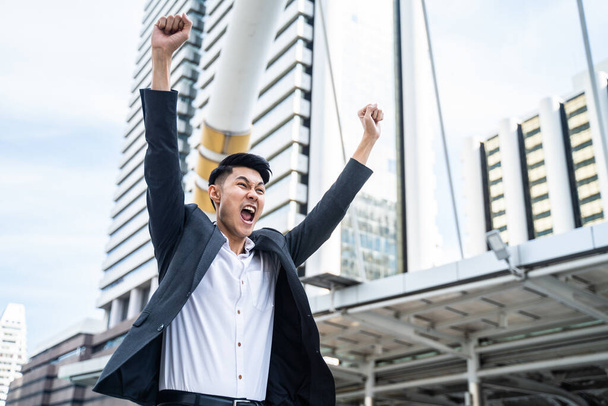 Asijský muž zvedne ruku se štěstím ve městě cítí rád, že dostane novou práci. Mladý podnikatel se cítí šťastný a volný poté, co věděl, že výsledek pohovoru pro žádost o zaměstnání je složen pro kancelářskou práci - Fotografie, Obrázek