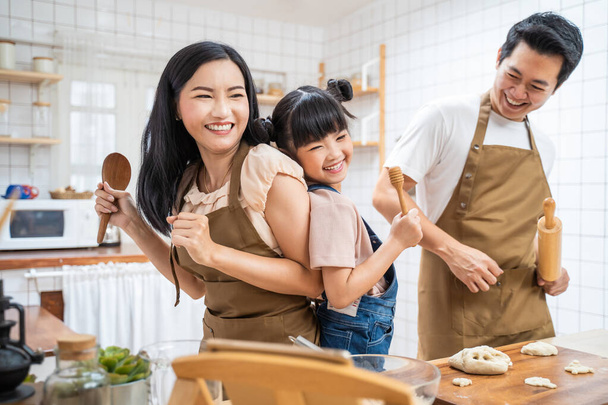 Azjatycka szczęśliwa rodzina pobyt w domu w kuchni piec piekarnię i tańczyć razem. Ojciec i matka spędzają wolny czas z młodą córeczką zrobić jedzenie, dziecko cieszyć się rodzicielstwo związek aktywność w domu. - Zdjęcie, obraz