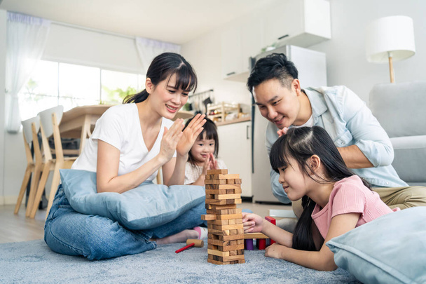 アジアの家族は家のリビングルームで一緒に休日に時間を過ごす。魅力的な幸せな両親、父と母は家の中で若い2人の子供の女の子の娘と木製のブロックおもちゃを再生します。活動関係. - 写真・画像