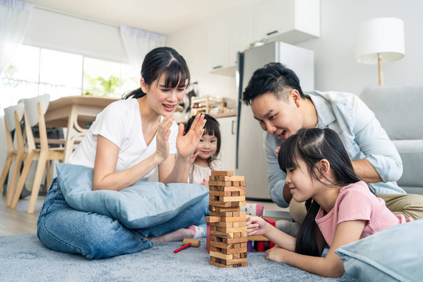 Azjatycka szczęśliwa rodzina siedzi na podłodze, bawi się w dziecięcą zabawkę w salonie. Atrakcyjny rodzic matka i ojciec cieszyć się aktywnością do gry upadek wieża blok drewna gra z młodymi córek cute girl w domu - Zdjęcie, obraz