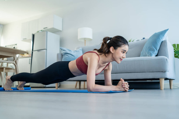 Asian Beautiful young woman stay home, doing cardio exercise at home. Attractive girl doing lockdown activity workout by plank on floor follow instruction video from online trainer for health in house - Photo, Image