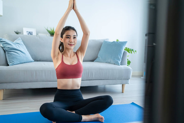 Asian young beautiful active woman doing Yoga Pilates workout at home. Attractive girl in sportswear feel happy and relax, follow exercise instruction video from online trainer in living room in house - Photo, image