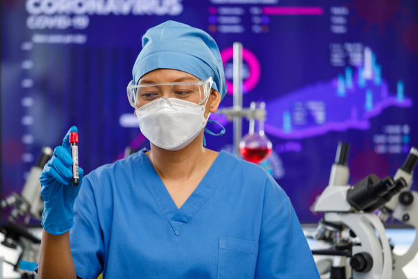 Ärztinnen mit Hygiene-Gesichtsmaske und Schutzglas bleiben im Laborraum und halten ein Probenreagenzglas mit Laborausrüstung im Hintergrund. - Foto, Bild