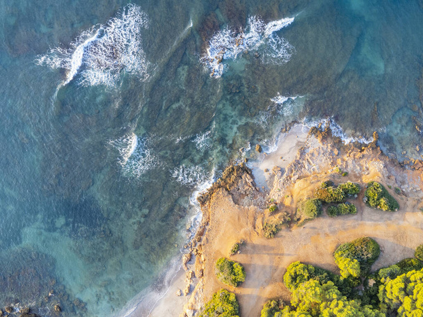 An aerial view of a rocky beach, a coastline with the waves crashing on the rocks at the seashore - Zdjęcie, obraz