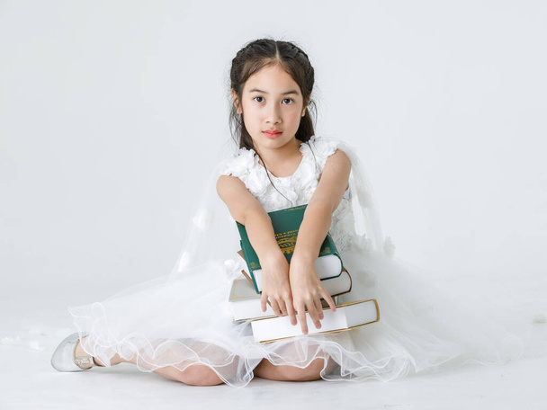 Portret studio shot van Aziatische mooi meisje draagt witte prinses lange roos bloem jurk mode kostuum poseren met stapel boeken op witte achtergrond. - Foto, afbeelding