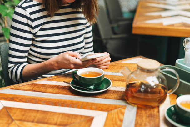 Młoda brunetka w ubraniu casual za pomocą mediów społecznościowych na telefon komórkowy siedzi w kawiarni - Zdjęcie, obraz
