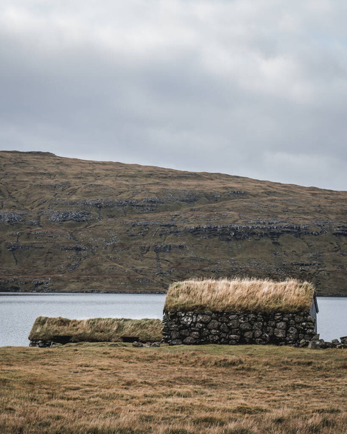 House from stones with grass rooftop, Faroe Islands. View of typical turf-top houses. Panoramic autumn scene of Faroe Islands. Moody dark landscape - 写真・画像