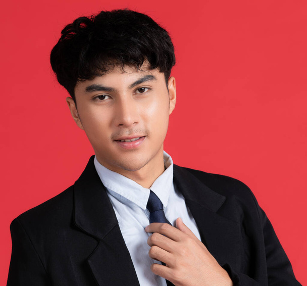 Muotokuva nuori fiksu ja komea aasialainen mies blck puku poseeraa ystävällinen kasvot ja itseluottamusta ele punaisella taustalla . - Valokuva, kuva