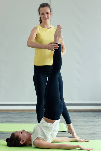 Eine Yoga-Meisterin in guter Form hilft dem Neuling, grundlegende Gesten zu üben und die Körperhaltung zu korrigieren. Konzept für das Erlernen neuer Fertigkeiten im Unterricht für Gesundheit und Geist. - Foto, Bild